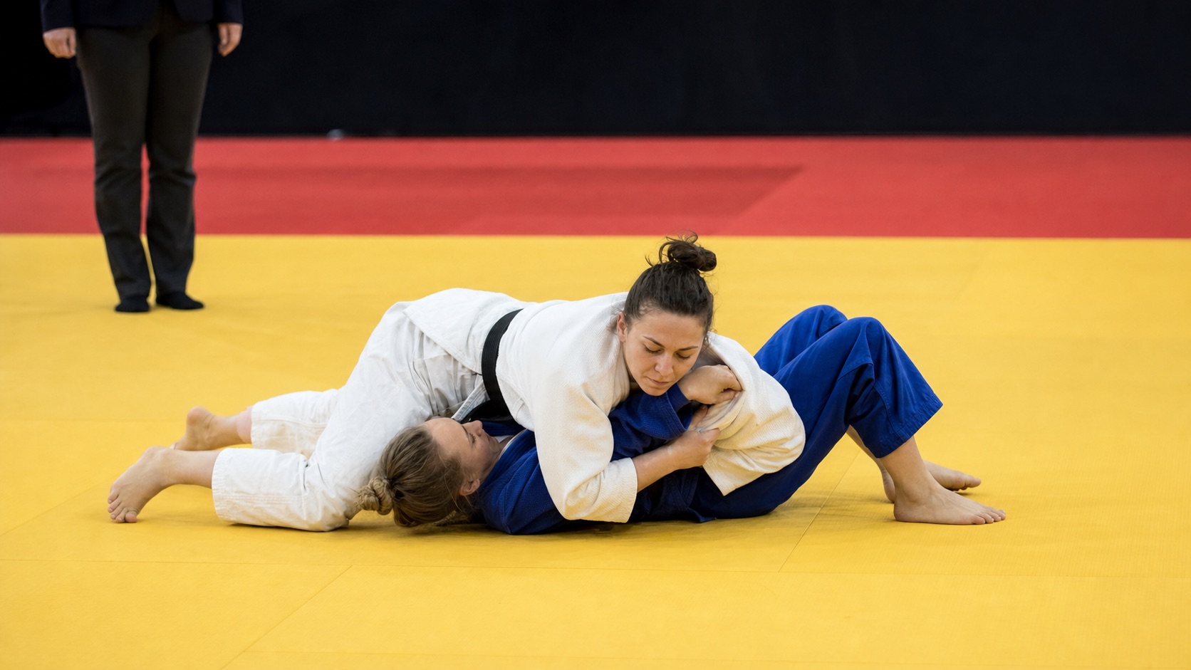 兩名女子柔道選手在榻榻米上進行寢技壓制對抗。